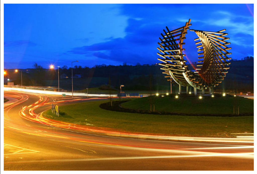 A circular star like structure constructed in wood, with the blurred lights of traffic in foreground