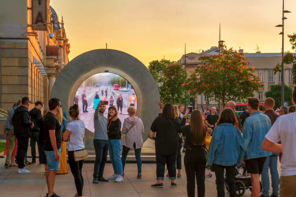 A group of people gather in front of a Portal artwork to get a glimpse of onlookers in a different location.