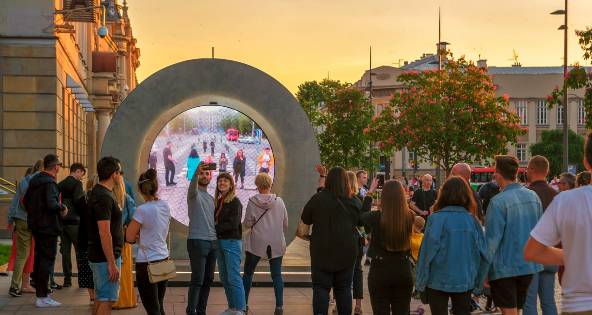 A group of people gather in front of a Portal artwork to get a glimpse of onlookers in a different location.
