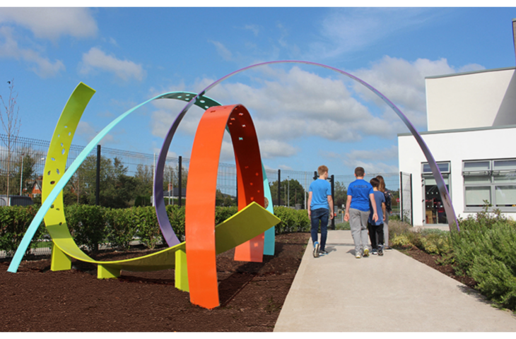 Students walk along a path next to a geometric piece of art in painted metal