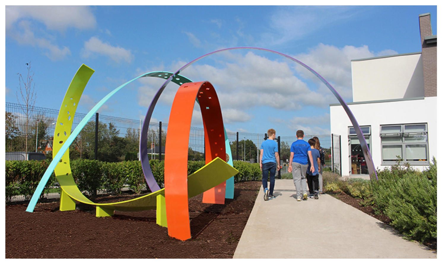 Students walk along a path next to a geometric piece of art in painted metal