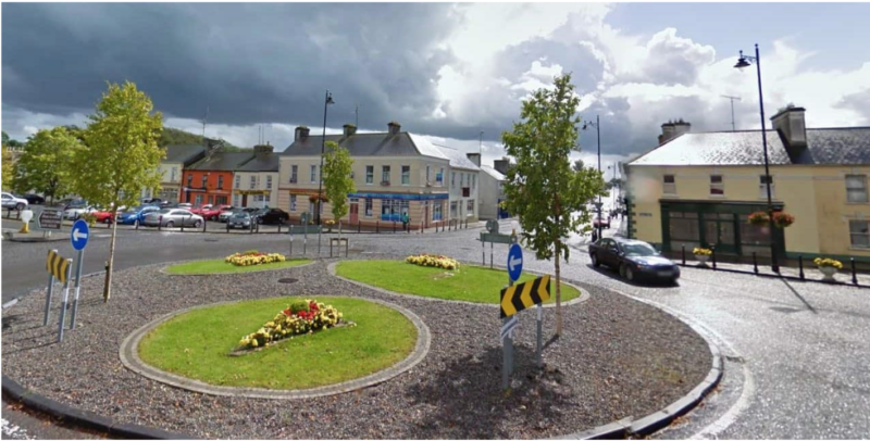 A town centre with green landscaping, houses, trees and a blue sky with clouds in the background